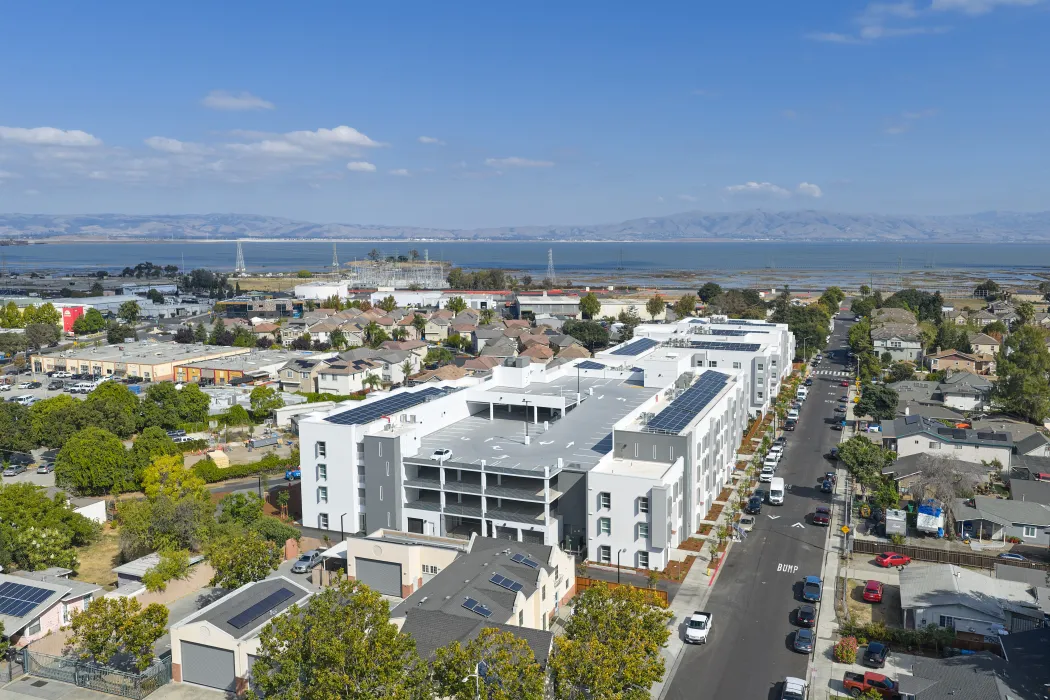 Aerial view of large white building set in an urban context showing entry to multilevel parking garage