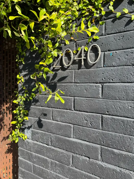 Black brick wall with plantings slightly obscuring metal building number 2040 in a san serif font