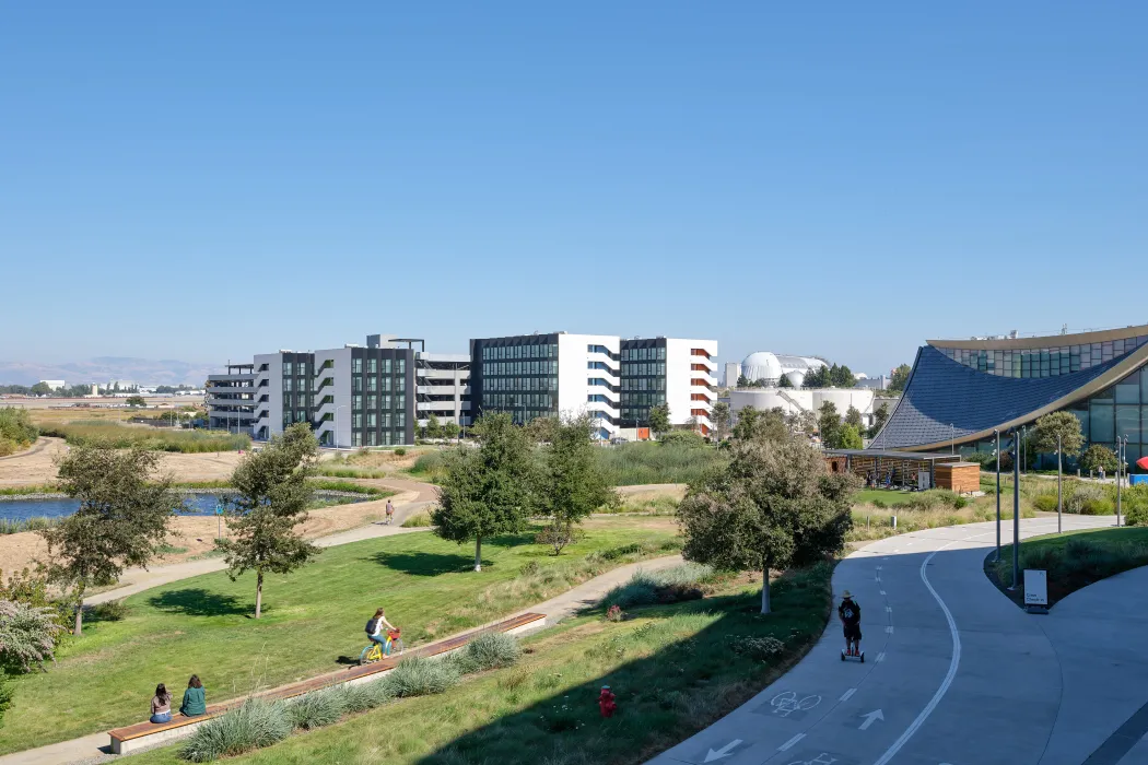 Large gray and white building with park and bike path in foreground and blue sky