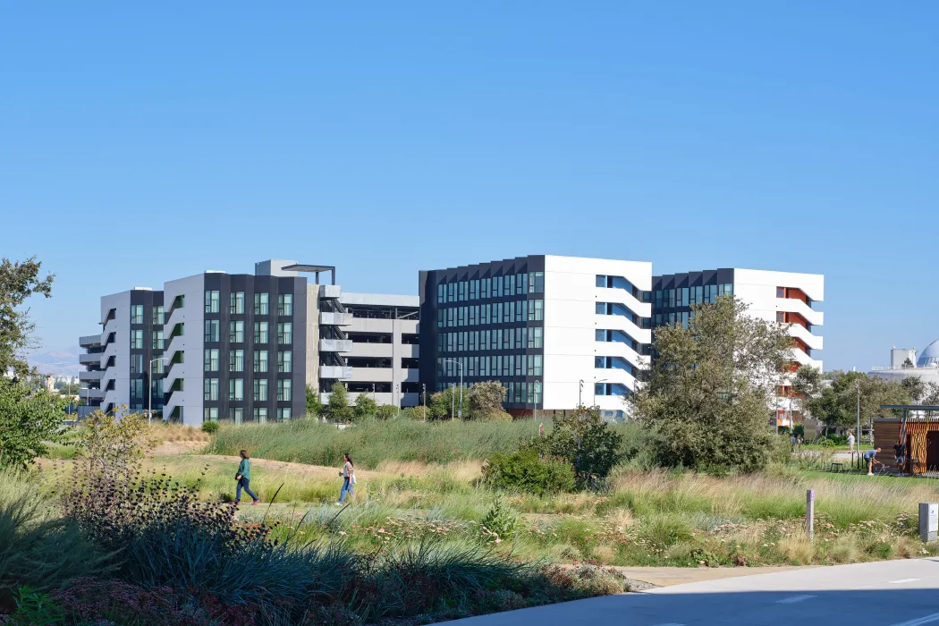 Large gray and white building against blue sky with park and bike path in foreground 