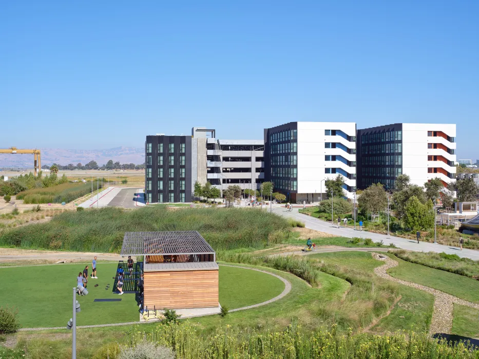 Large gray and white building with small building with wood siding in a park in foreground against blue sky
