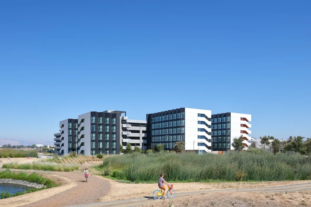 Large gray and white building against blue sky with bike path in the foreground