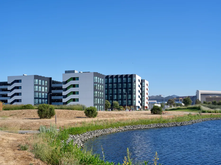 Large gray and white building against blue sky with a lake in foreground 