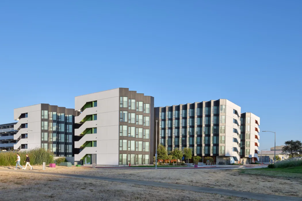 Large gray and white building against blue sky with bike path in foreground 