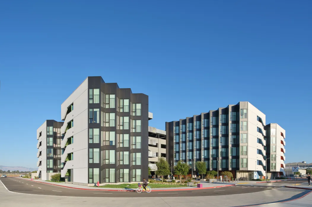 Large gray and white building with park and bike path in foreground and blue sky