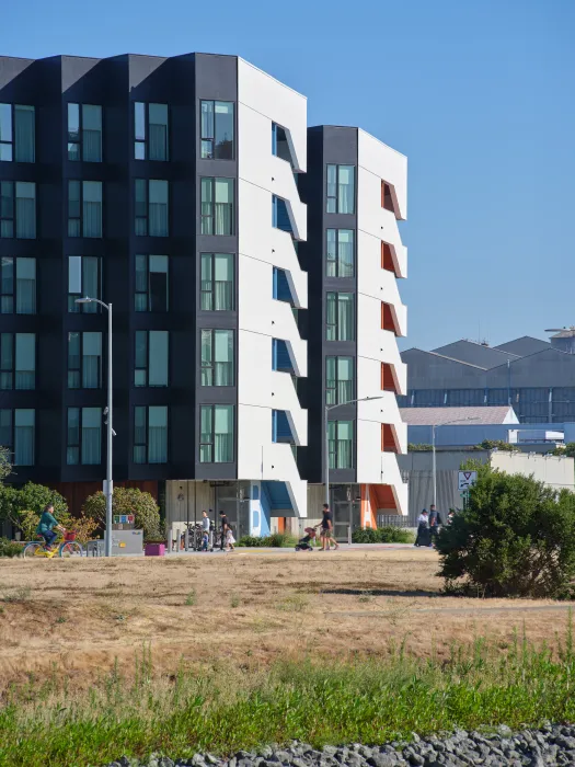 Large gray and white building with park and bike path in foreground and blue sky