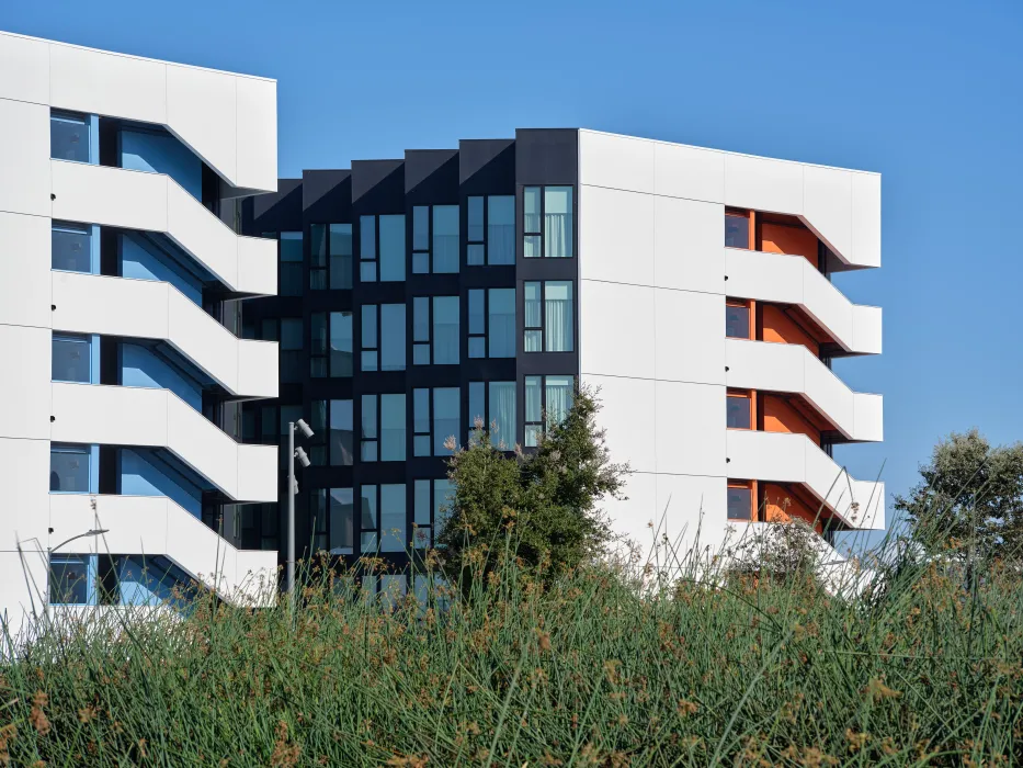 Gray and white building with orange and light blue accents against blue sky and green landscape in the foreground