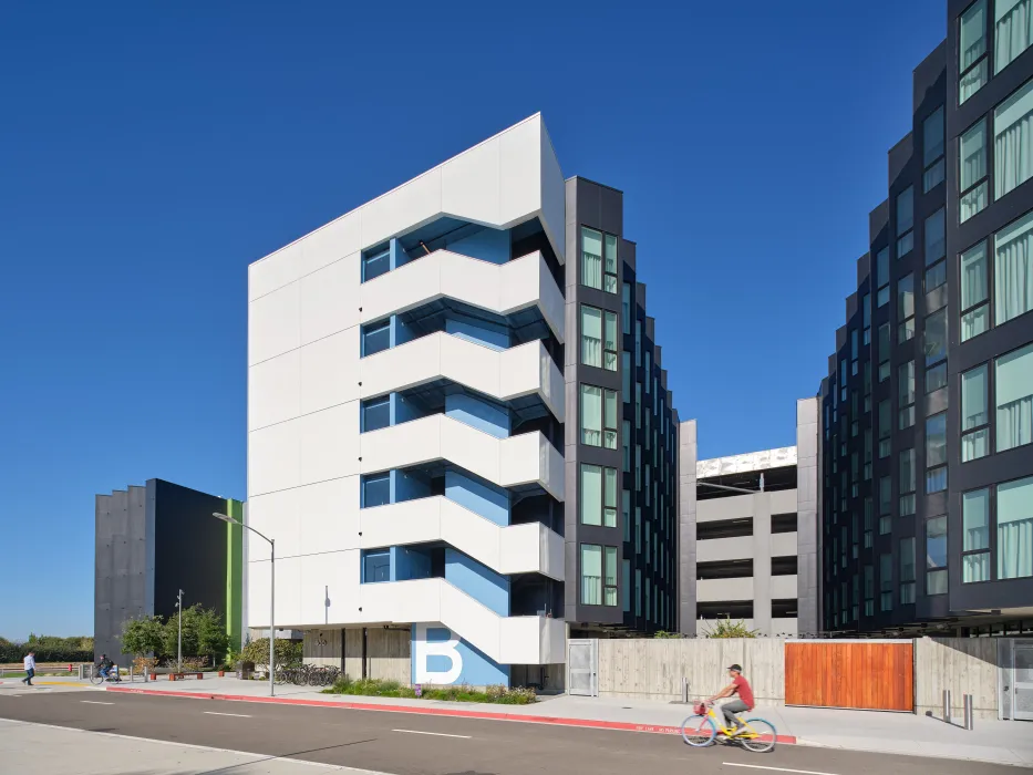 Large gray and white building with bike path in foreground and blue sky