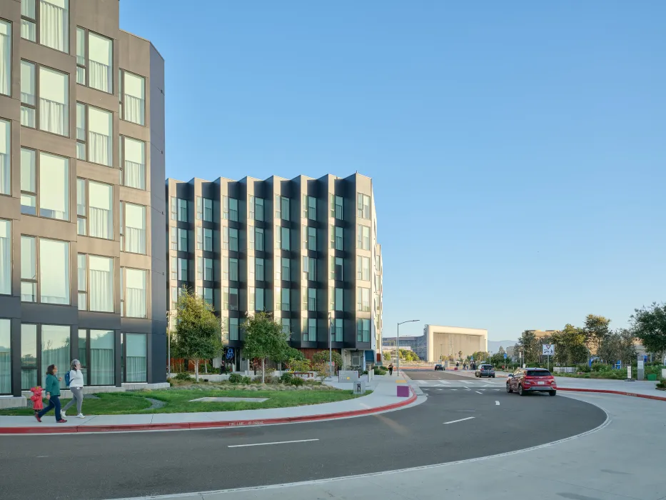 Gray buildings against a blue sky with cars on road in front