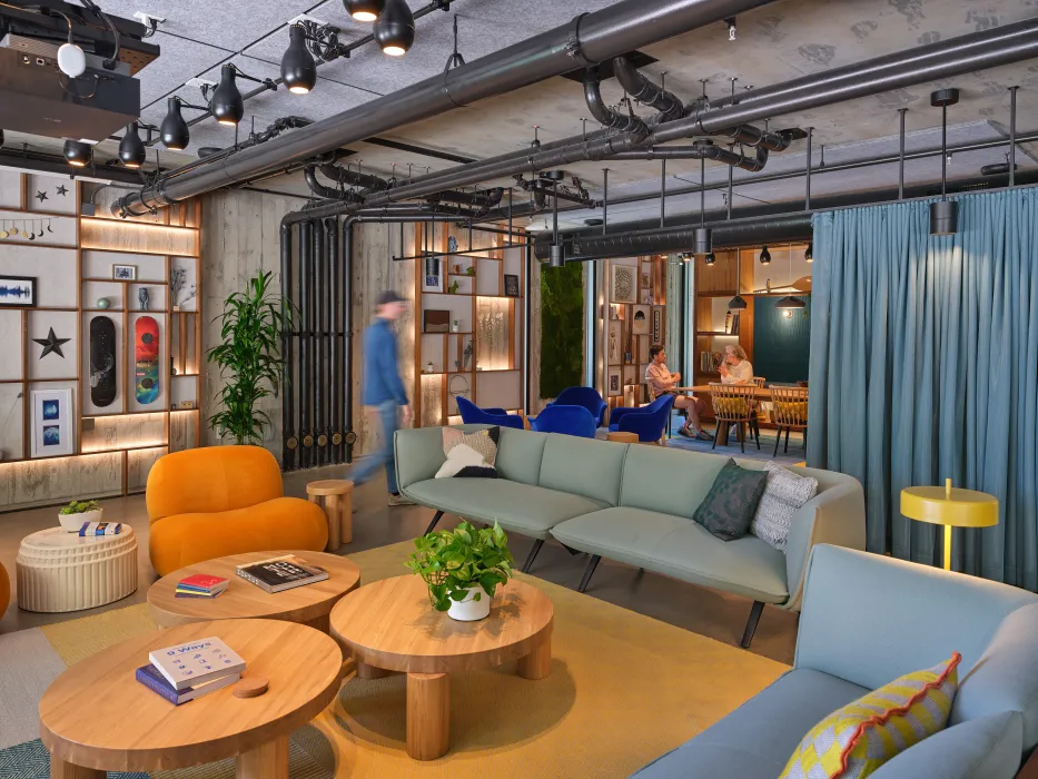 Lounge space with 2 sofas and 3 round tables with blue curtain and conference room in background