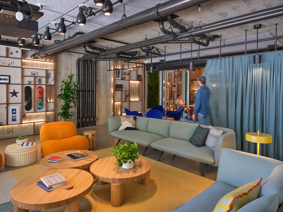 Lounge space with 2 sofas and 3 round tables with blue curtain and conference room in background