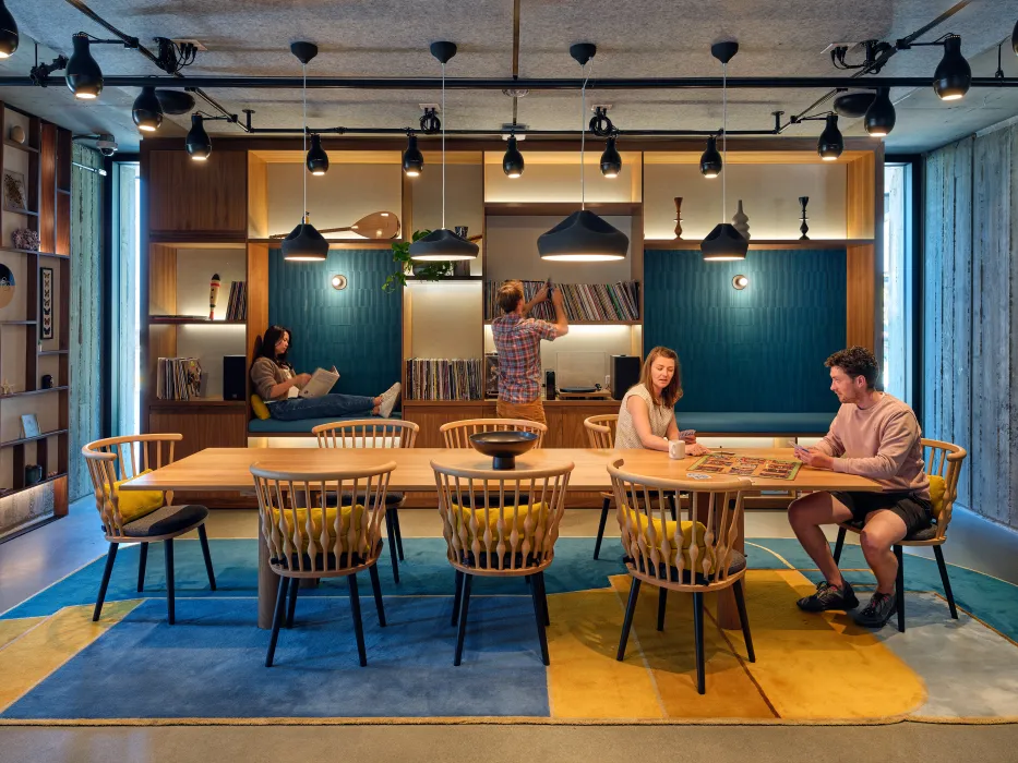 Room with blue and yellow rug and two people sitting at large rectangular table