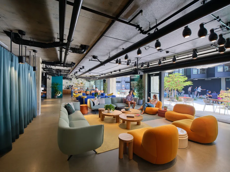 Lounge area with blue sofas, orange chairs and a blue curtain looking to outdoor space through open garage doors