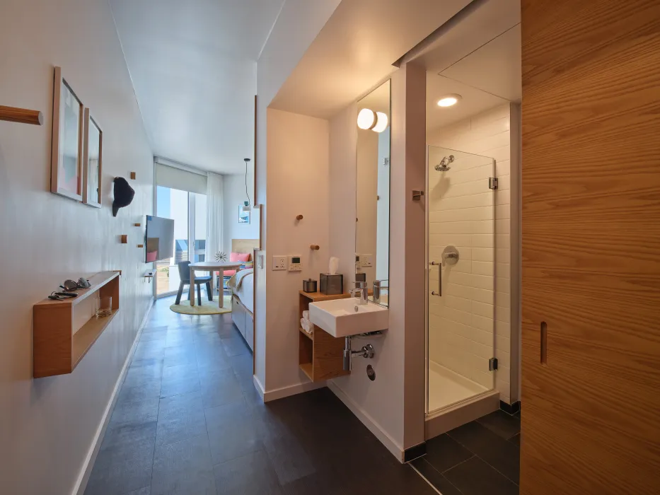 Interior suite with seating area and sliding door in background and white bathroom sink and shower in foreground