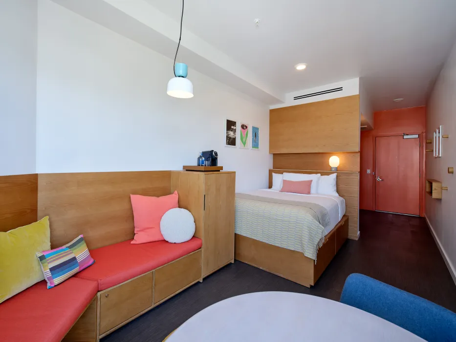 Bedroom studio with built in wooden bed and seating area with red cushion  