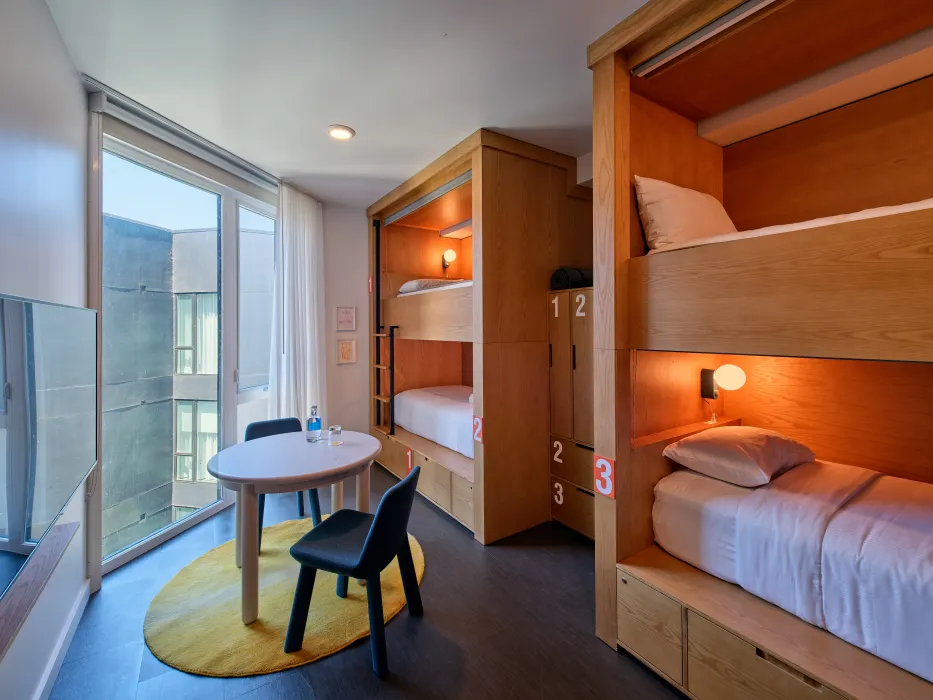 Bedroom with four wooden built-in bunk beds, yellow rug and large window
