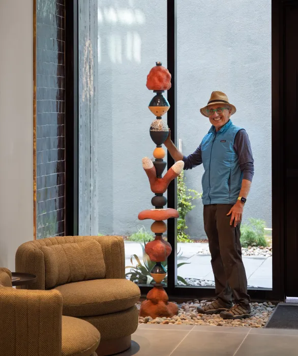 Man in hat and blue vest posing with ceramic sculpture