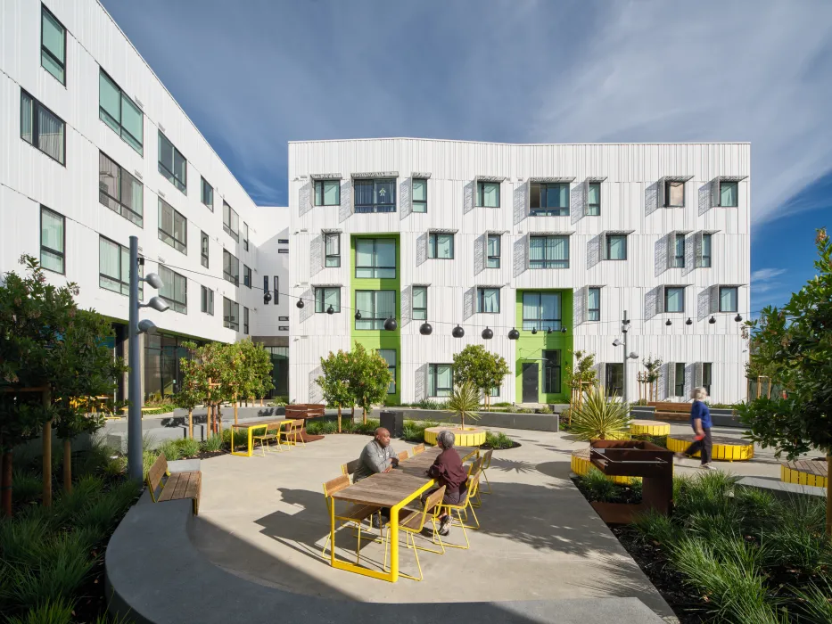 Exterior of white apartment building with green entry portals; seating in foreground