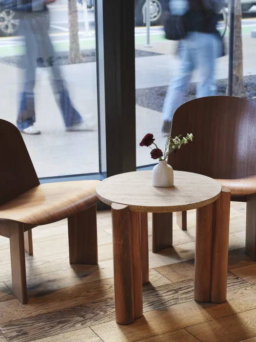 Detail shot of two chairs and a low table in front of window; passersby visible outside