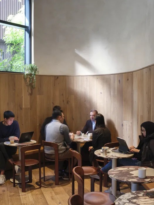 People having coffee and working on laptops at tables along the curving wood wall
