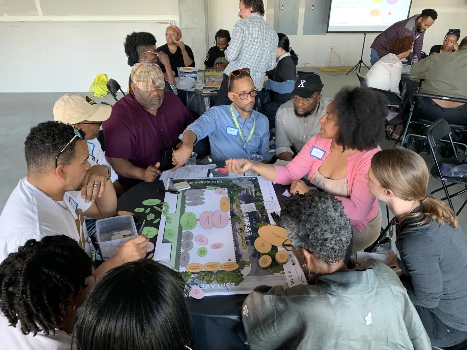 A group of people are gathered around a site and buidling plan and gesturing in discussion with sticky notes