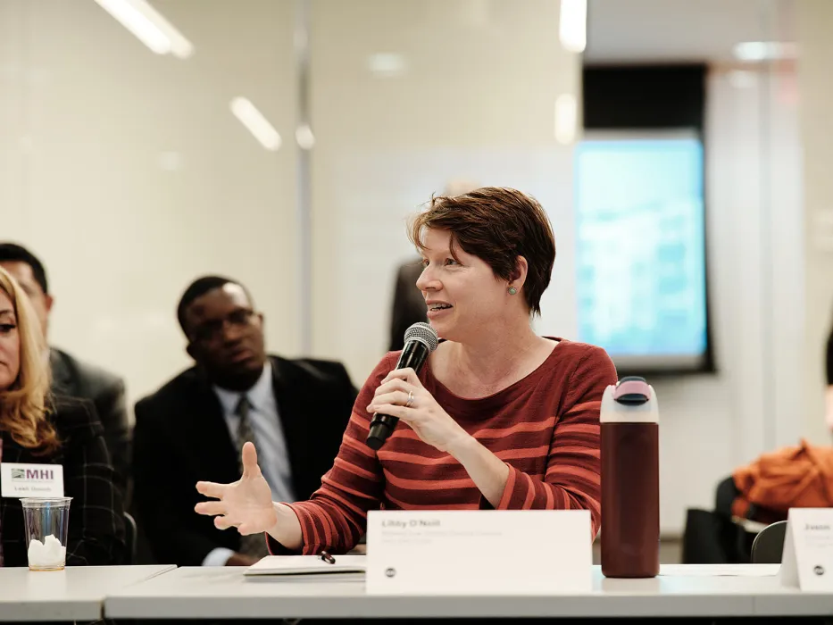 Woman in rust-colored sweater speaks with a microphone