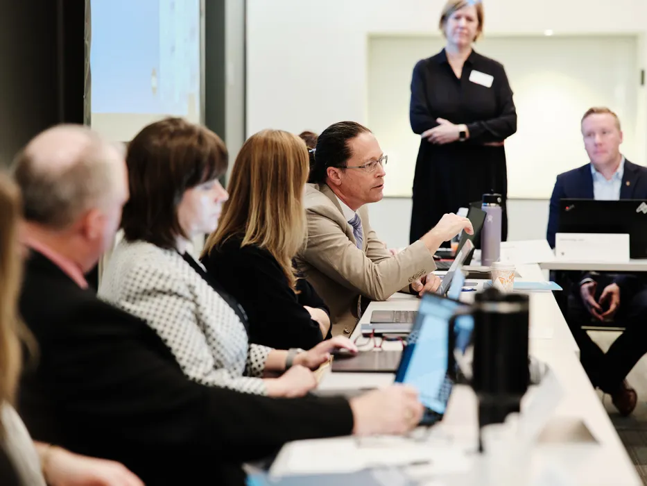 Group of people seated at long table, speaking