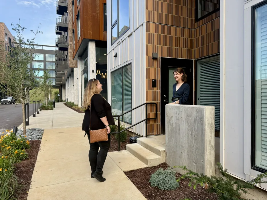 Two people talking on stoop of building with crosswalk in background 