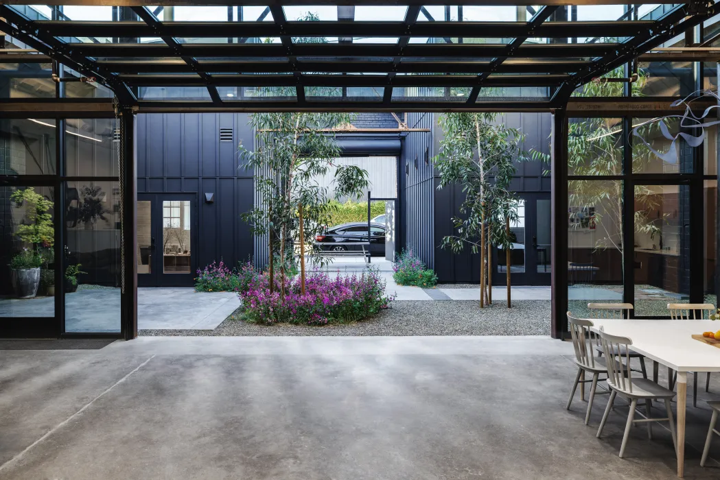 Large black steel framed room with glass and garage door opening to courtyard with trees
