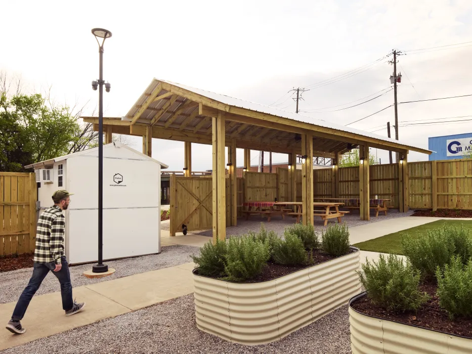 A man in a checked shirt and jeans walks past raised garden beds
