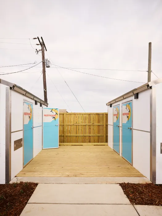 Two small structures with four doors marked with restroom signs share a wooden deck