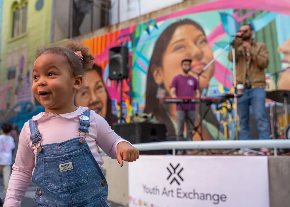 Young girl in courtyard in front of musicians and colorful mural