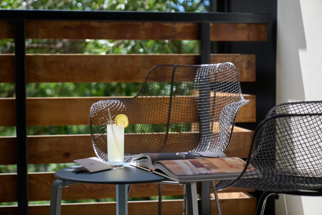 Closeup shot of a glass of lemonade with a lemon slice on a shady balcony with a wire chaire