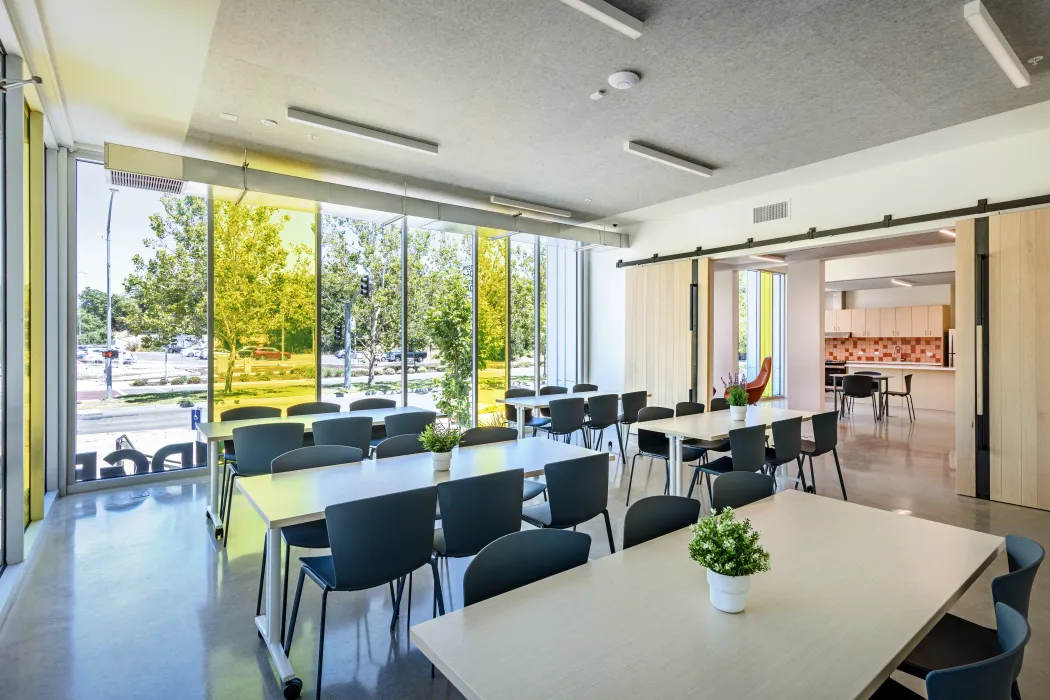Interior of a community room with conference tables and chairs and a floor-to-ceiling window with clear and yellow glass
