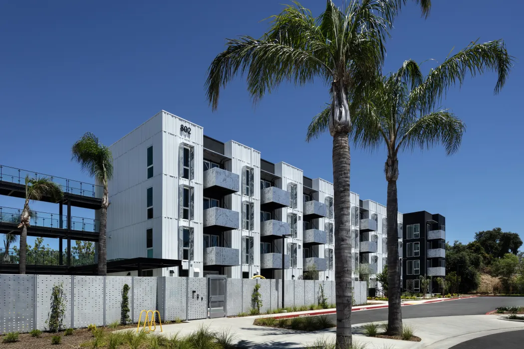 Daytime view of rear of multifamily building with palm trees and perforated-aluminum balconies