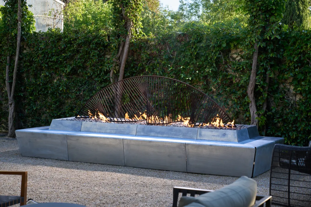 Sculptural concrete and steel fire feature with flames in front of ivied wall