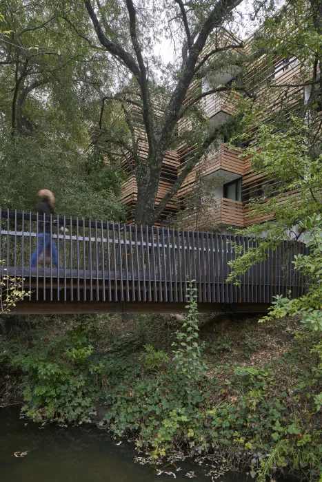 An image of a woman crossing a shaded wooden bridge over a creek.